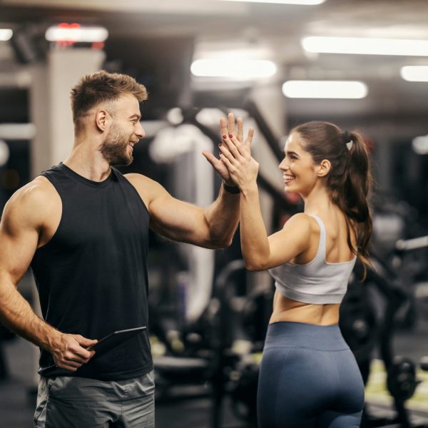 A fit sportswoman giving high five to her personal trainer in gym.