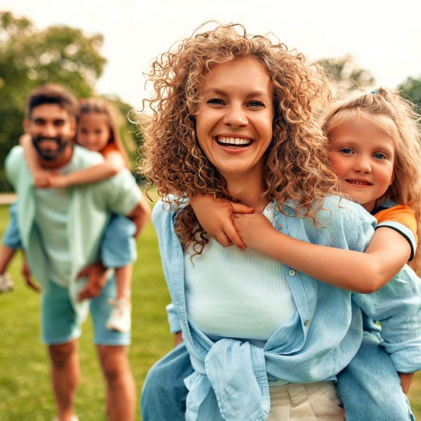 Happy young family father, mother and two daughters playing in the meadow in the park on a warm sunny day, having fun together and relaxing on a day off.